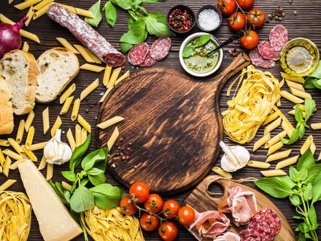 Top view of Italian traditional food, appetizers and snacks as salami, prosciutto, cheese, pesto, ciabatta, olive oil, pasta on rustic wooden round board with space for text in centre