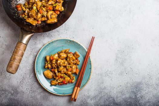 Top view of Kung Pao chicken on plate ready for eat, space for text. Stir-fried Chinese traditional dish with chicken, peanuts, vegetables, chili peppers. Chinese dinner, chopsticks, stone background