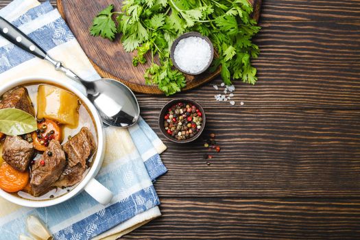 Close-up of slow cooked meat stew ragout in bowl with beef, potato, carrot, broth on wooden rustic background, top view with space for text. Hot homemade food for dinner, meat casserole copy space.