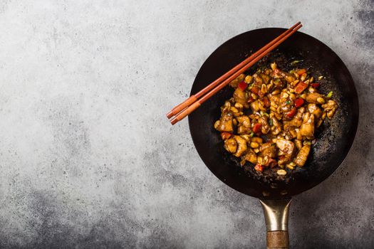 Top view of Kung Pao chicken, stir-fried Chinese traditional dish with chicken, peanuts, vegetables, chili peppers in a wok pan, space for text. Chinese dinner, chopsticks, rustic concrete background