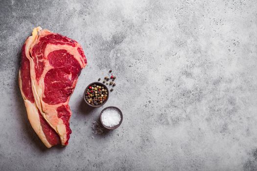 Top view of raw marbled juicy meat beef Rib eye steak ready for cooking, with seasonings, grey concrete rustic background, space for text