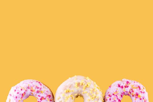 pink and yellow spricled donuts on a yellow background Space for text high-quality photos for calendar and cards