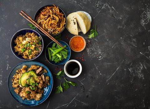 Asian assorted food set, dark rustic stone background. Chinese dishes. Chinese stir-fry noodles, asian rice with meat, dim sum, snacks, steamed Chinese buns. Space for text. Top view. Asian style