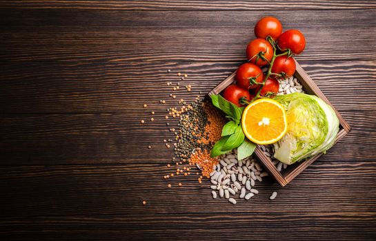 Top view of healthy diet food ingredients in wooden box: vegetables, beans, fruit, herbs with space for text, rustic wooden background. Food ingredients for healthy vegetarian dinner