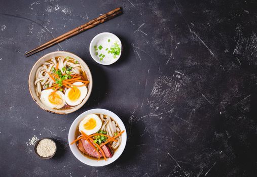 Bowls with Japanese soup ramen, chopsticks, black concrete rustic background. Traditional Asian soup with noodles, meat, broth, eggs. Asian food. Japanese ramen for dinner. Ramen, close-up. Overhead.