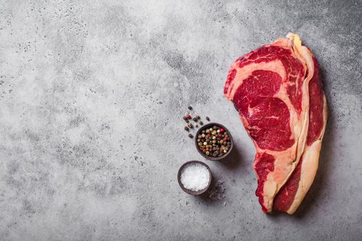 Top view of raw marbled juicy meat beef Rib eye steak ready for cooking, with seasonings, grey concrete rustic background, space for text