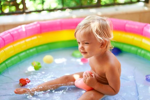 Little girl sits in a pool on the balcony with a toy. High quality photo