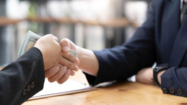 An Asian female lawyer or business legal consultant at the office desk receives money and shaking hand with her male client. cropped image.