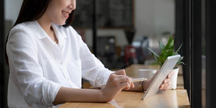 Beautiful young Asian woman or female college student relaxes sitting in the coffee shop and using portable tablet touchpad..