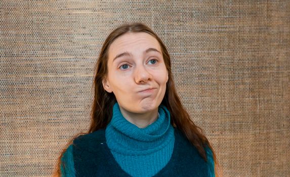 a red-haired girl in a green warm suit against a straw wall laughs skeptically or makes faces