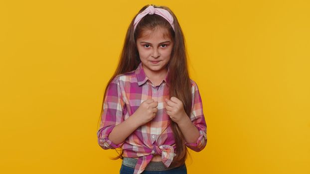 Aggressive preteen child girl kid making fight threat at camera, shaking fist punch, boxing with expression, punishment practicing exercises negative rage. Little toddler children on yellow background