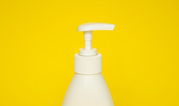 White plastic soap or shampoo dispenser pump bottle isolated on yellow background. Skin care lotion. Bathing essential product. Shampoo bottle. Bath and body lotion. Fine liquid hand wash