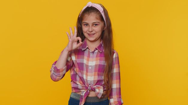 Ok. Happy cheerful preteen child girl looking approvingly at camera showing ok gesture, positive like sign, approve something good. Little toddler children kid isolated on studio yellow background