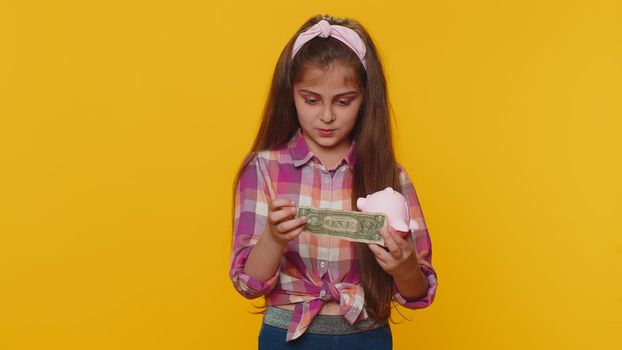 Poor young preteen child girl kid insufficient amount of money, holding piggybank and one dollar banknote at home. Financial crisis. Bankruptcy. Poverty and destitution. Little toddler children alone