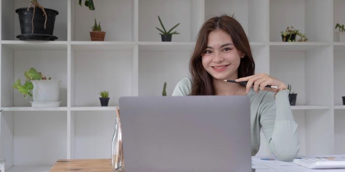 Charming Asian woman working at the office using a laptop Looking at the camera..