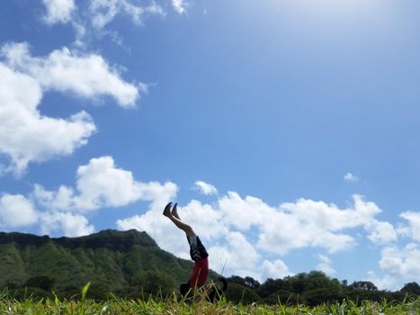 Man Handstanding in Kapiolani Park at during day with Diamond Head and clouds in the distance on Oahu, Hawaii.