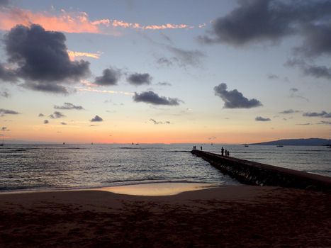 Rock Pier leading into Pacific ocean at dusk with boats off the coast of Oahu, Hawaii with Waianae Mountain range visible. February 2016.