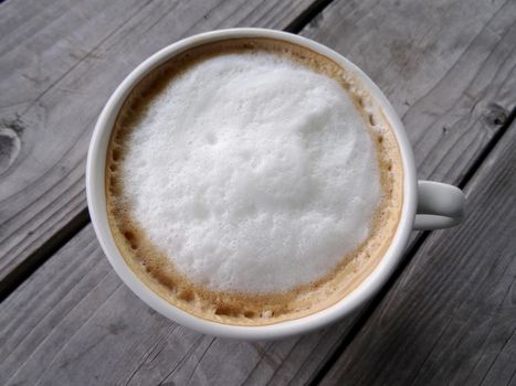 White cup of Cappuccino with a Large white dot of foam on wood table.