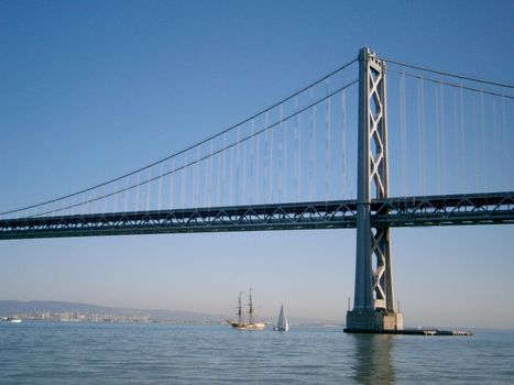 Boats sail under the San Francisco side of Bay Bridge with Oakland in the distance on a clear day.