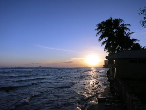 Sunsets over Waikiki waters as waves roll towards sea wall at Leahi Beach Park on Oahu, Hawaii.