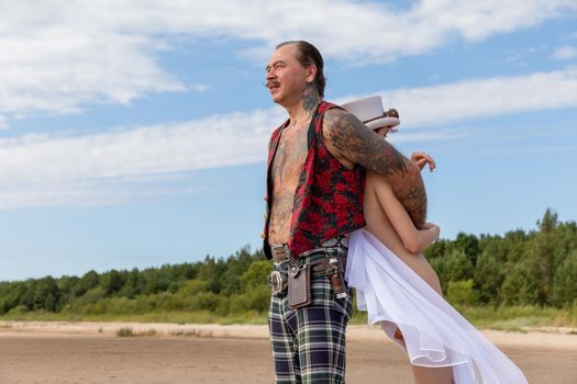 AINAZI, LATVIA – Jul 29, 2019: Love story. Non-traditional wedding photo shoot on the shores of the Baltic Sea. Nude bride in a veil and a spectacular groom