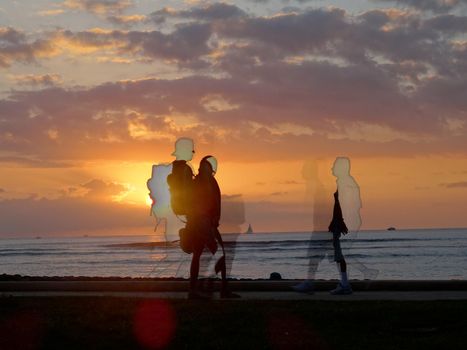 Waikiki - January 16, 2016:  Sunset dropping behind the ocean on Kaimana Beach and images of people walking by with boats on the water on Oahu, Hawaii.