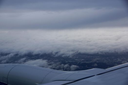 Wing of plane flies over City of Seattle, Washington covered in clouds.