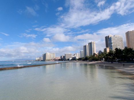 Waikiki - August 13, 2015: People play in the protected water and hang out on the Kuhio Beach in world famous tourist area Waikiki on a beautiful day with hotels in the distance.  Family-friendly Waikiki beach park with shallow, lagoon-like water & statues honoring local legends.