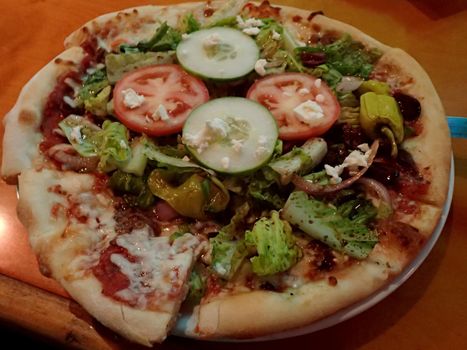 VEGGIE PIE - Veggie Pizza featuring Red sauce, cucumbers, lettuce, onion, peppers and cheese on a table.