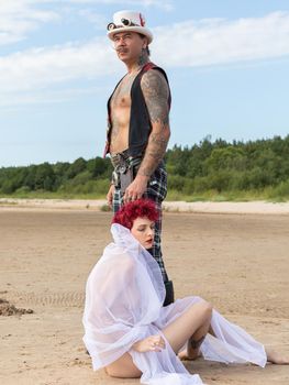 AINAZI, LATVIA – Jul 29, 2019: Love story. Non-traditional wedding photo shoot on the shores of the Baltic Sea. Nude bride in a veil and a spectacular groom