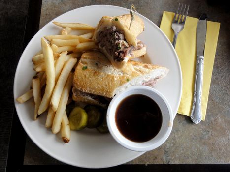 french dip sandwich.  In American cuisine, the French dip sandwich, also known as a beef dip, is a hot sandwich consisting of thinly sliced roast beef on a "French roll" or baguette. It is served topped with Swiss Cheese, onions, and a side of sauce, pickles, and that is, with beef juice from the cooking process.