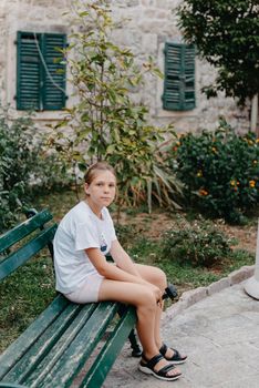 Girl Tourist Resting in the Ancient Narrow Street On A Beautiful Summer Day In MEDITERRANEAN MEDIEVAL CITY, OLD TOWN KOTOR, MONTENEGRO. Young Beautiful Cheerful Woman Walking On Old Street