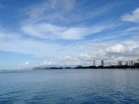 Glassy water of Ala Moana Beach with Condo buildings and construction cranes in the distance during a beautiful day on the island of Oahu, Hawaii. 