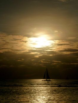 Sunsets through the clouds with light reflecting on ocean and illuminating the sky with boats sailing on the water off Waikiki on Oahu, Hawaii.