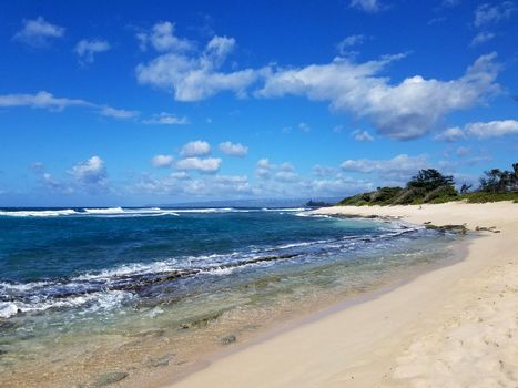 Rocky beach with Shallow wavy ocean waters of Camp Mokuleia Beach looking into the pacific ocean with a clear blue sky on Oahu.