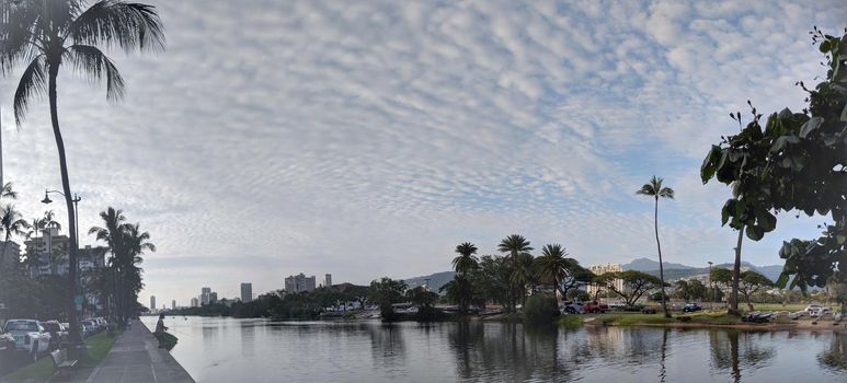 Ala Wai Canal, man fishing, hotels, Condos, Golf Course and Coconut trees at dusk on a nice day in Waikiki on Oahu, Hawaii with mountains in the distance.