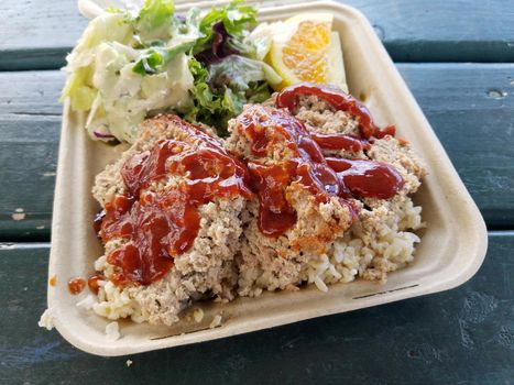 Turkey Meatloaf Plate Lunch with Brown rice, salad, and orange slice on green table.