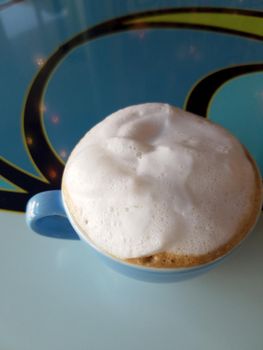 Blue cup of Cappuccino on saucer with large top of  foam on table.