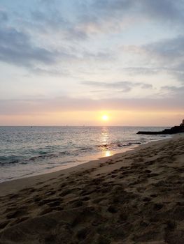 Sunsets over Waikiki waters as waves roll into shore at Makalei Beach Park with sail boats in the ocean on Oahu, Hawaii.