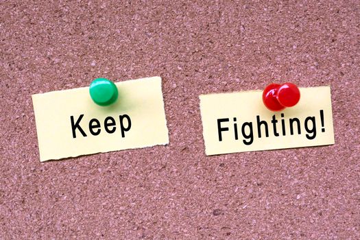 Keep fighting words on stick note and blue pinned to a cork notice board. Business concept.