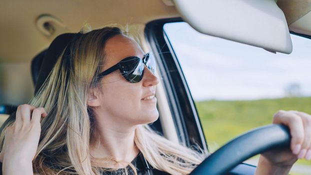 A young woman in a good mood behind the wheel of a car