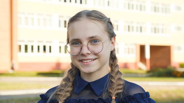 A teenage girl wearing glasses in front of a school