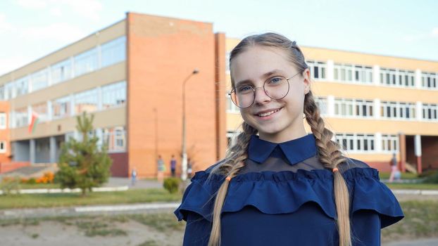 A teenage girl wearing glasses in front of a school