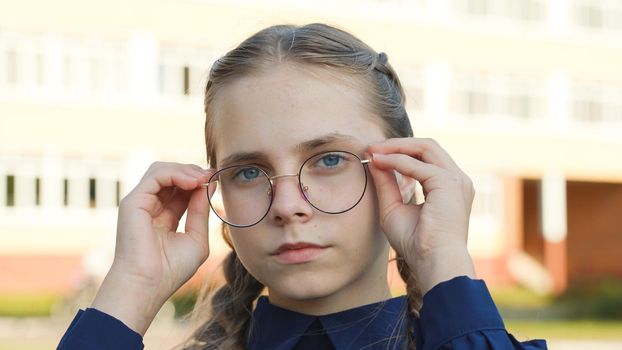 A teenage girl wearing glasses in front of a school