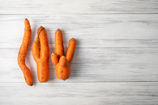 Top view close-up of several ripe orange ugly carrots lie on a light wooden surface with copy space for text. Selective focus.