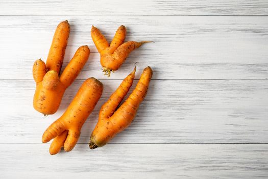 Top view close-up of several ripe orange ugly carrots lie on a light wooden surface with copy space for text. Selective focus.