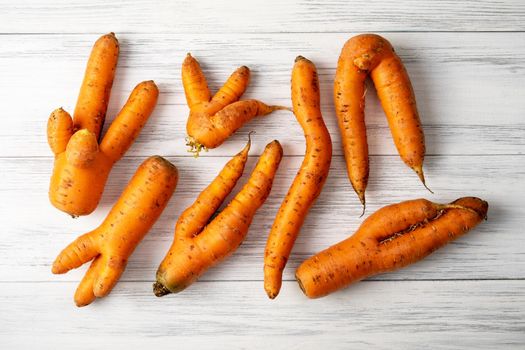 Top view close-up of several ripe orange ugly carrots lie on a light wooden surface. Selective focus.