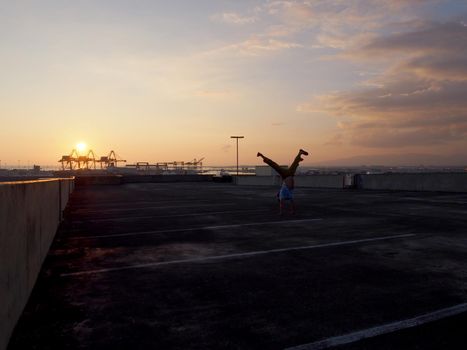 Man does Split leg Handstand on top floor of parking garage above the City of Honolulu on Oahu, Hawaii at Sunset. January 2016.