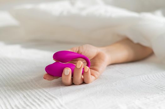 A faceless woman lies in bed under a blanket holding a clitoral vaginal vibrator. The girl masturbates.