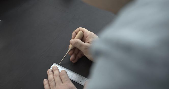 Close up of leather craftsman working with natural leather by awl and ruler. Handmade master at work in local workshop. Leather wallet stitch